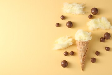 Waffle cone with cotton candy and chocolate sweets on beige background, flat lay. Space for text