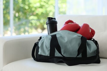 Stylish bag with sports equipment on sofa at home. Space for text
