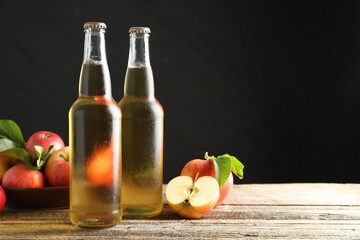 Delicious cider in glass bottles and apples on wooden table against dark gray background. Space for text