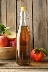 Delicious cider in glass bottle and apples on wooden table