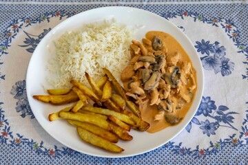 Delicious chicken stroganoff with rice and rustic roasted potatoes on a round white plate and a nice clean table setting