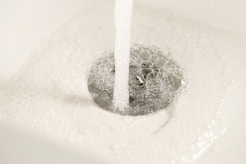 Water saving concept. Water going into sink drain, closeup