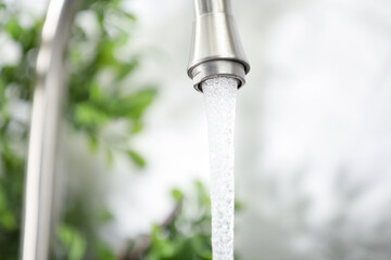 Water saving concept. Stream of water flowing from tap indoors, closeup