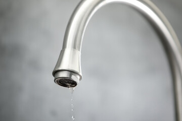 Save water concept. Water dripping from tap against grey background, closeup