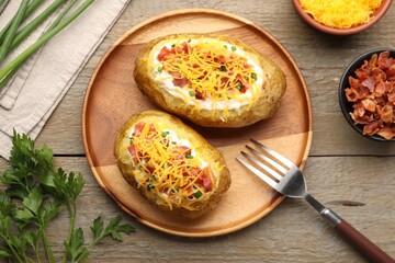 Tasty baked potatoes with sour cream, green onion, cheese and bacon served on wooden table, flat lay