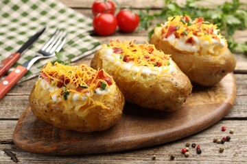 Tasty baked potatoes with sour cream, green onion, cheese, bacon and peppercorns on wooden table, closeup