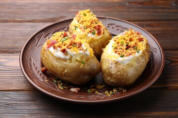 Tasty baked potatoes with sour cream, green onion, cheese and bacon on wooden table, closeup