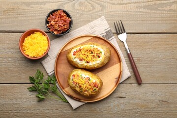 Tasty baked potatoes with sour cream, green onion, cheese and bacon served on wooden table, flat lay