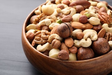 Mix of different nuts in bowl on black wooden table, closeup