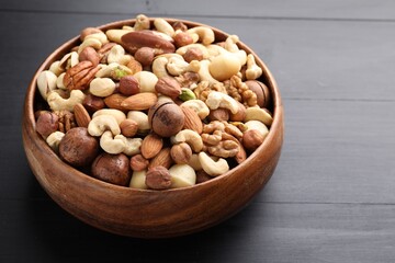 Mix of different nuts in bowl on black wooden table, closeup. Space for text