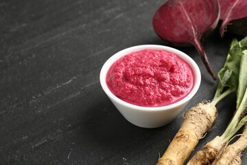 Tasty horseradish sauce with beetroot, roots and vegetable on black table, closeup. Space for text