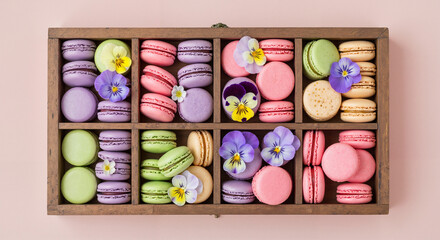 Colorful macarons arranged in a wooden box with edible flowers  