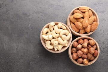 Different nuts in bowls on grey table, flat lay. Space for text