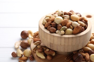 Mix of different nuts in bowl on white wooden table, closeup
