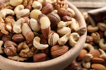 Mix of different nuts in bowl on wooden table, closeup