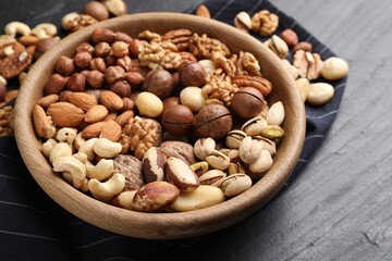Mix of different nuts in bowl on black table, closeup