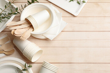 Set of disposable tableware and eucalyptus branches on light wooden table, flat lay. Space for text