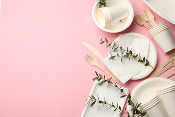 Set of disposable tableware and eucalyptus branches on pink background, flat lay. Space for text