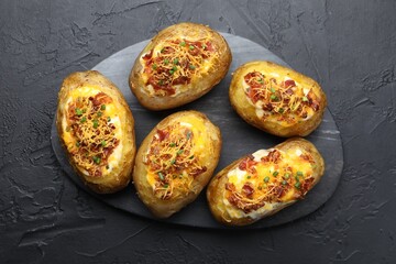 Tasty stuffed baked potatoes on black textured table, top view