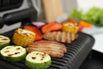 Electric grill with tasty meat and vegetables in kitchen, closeup