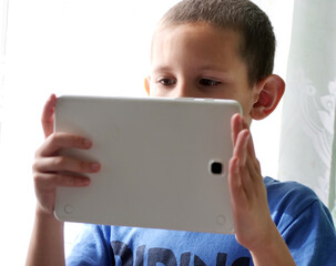 Boy watching a screen on a tablet - A Young Boy Looking Intently at the Screen of a White Tablet