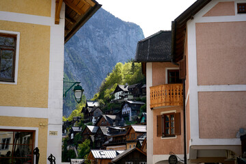 Pastel facades frame a hillside cluster of wooden cottages below a sheer rock wall. A green bracket lamp and carved balcony add crafted detail to a quaint mountain settlement in bright spring light. © VladyslavShcherbakov