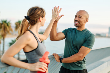 Smiling active young couple jogging exercising and having fun and laughing together taking a break after walking and running in the park, high five exchange