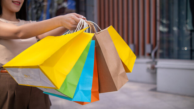 A young Asian woman holds several colorful shopping bags in her hands after going shopping in a shopping mall because of a holiday sale. Many colorful shopping paper bags in the hands of a young woman