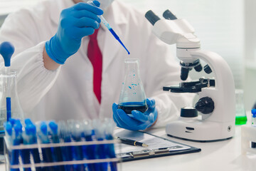 Fototapeta premium medical or scientific researcher researching and experimenting Multi-colored solution, vial and microscope In the laboratory or in the laboratory by wearing blue gloves and white clothing completely.