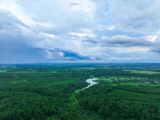Obraz premium A wide aerial view of a winding river in the middle of a dense green forest, with a stormy, dark cloudscape above it.