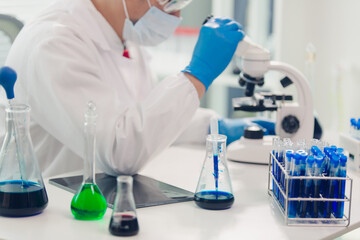 Fototapeta premium medical or scientific researcher researching and experimenting Multi-colored solution, vial and microscope In the laboratory or in the laboratory by wearing blue gloves and white clothing completely.