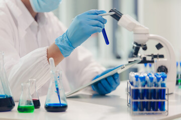 Fototapeta premium medical or scientific researcher researching and experimenting Multi-colored solution, vial and microscope In the laboratory or in the laboratory by wearing blue gloves and white clothing completely.