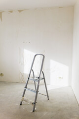 Ladder in a room undergoing renovation with white walls and sunlight