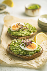 Toast with avocado, feta cheese, eggs, herbs and seeds with lemon slices on white background. Healthy eating and wholesome Breakfast