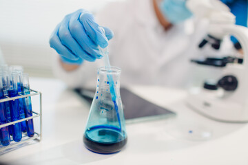 medical or scientific researcher researching and experimenting Multi-colored solution, vial and microscope In the laboratory or in the laboratory by wearing blue gloves and white clothing completely.