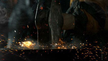 Fototapeta na wymiar Close-up of blacksmith forging glowing hot iron on anvil with flying sparks