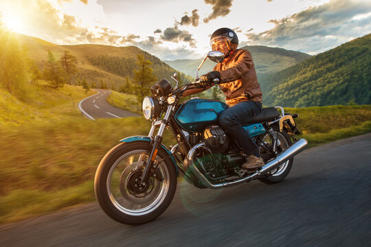 Driver riding motorcycle on empty road during sunset, spring mountains