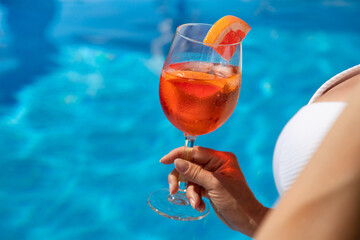 Beautiful brunette woman in a hat sitting and enjoying cocktail at swimming pool