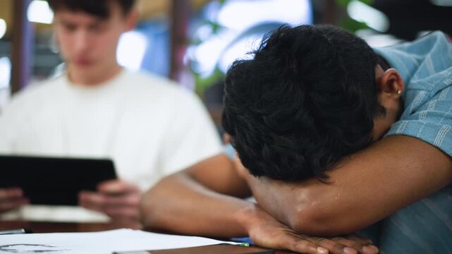 Closer view of lad with bob haircut leaning over wooden table supporting face with elbows conveying introspective mood in warm indoor light with blurred background capturing candid portrait moment