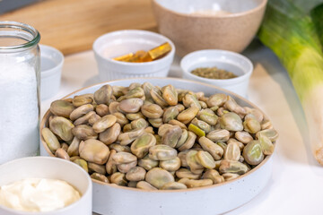 Fresh organic fava beans in a white bowl surrounded by natural ingredients, showcasing healthy nutrition and vibrant colors in a rustic kitchen setting with copy space