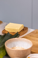 Fresh butter block on a wooden serving board surrounded by cooking ingredients, showcasing food preparation and culinary creativity in a modern kitchen setting