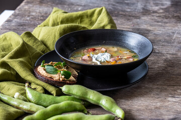 Fresh vegetable soup served in a black bowl alongside a slice of bread topped with creamy spread and garnished with herbs, showcasing healthy cooking and nutrition concepts
