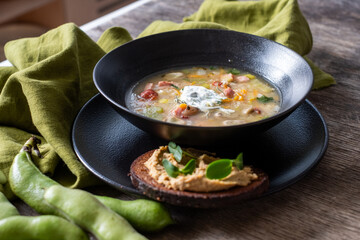 Fresh vegetable soup served in a black bowl with a dollop of cream, accompanied by a slice of bread, garnished with herbs, showcasing healthy cooking and nutrition concepts