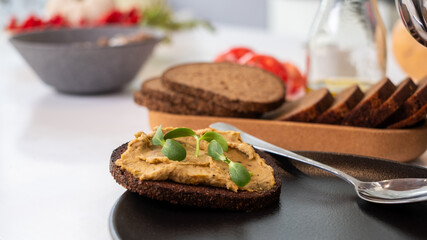 Freshly baked full grain bread topped with creamy hummus and sprouts, presented on a dark plate with copy space for healthy eating inspiration