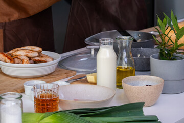 Fresh ingredients including chicken, milk, and vegetables are arranged on a kitchen counter, showcasing the cooking preparation process with vibrant colors and textures