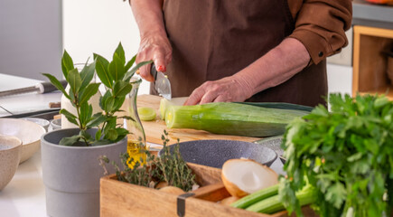 Chef skillfully chopping fresh leeks on a wooden cutting board surrounded by vibrant herbs and ingredients, showcasing creativity and technique in home cooking