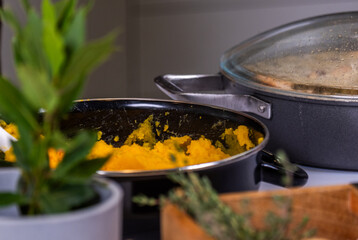 Freshly prepared pumpkin puree in a black pot, surrounded by aromatic herbs and plants, showcasing healthy autumn harvest and natural nutrition concept with copy space