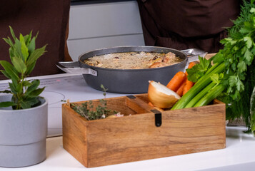 Fresh vegetables and herbs arranged beside a pot of healthy stew on a modern kitchen countertop,...