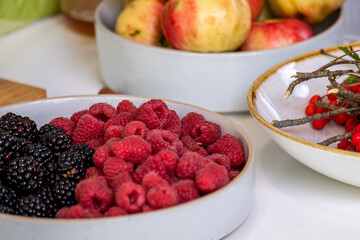 Fresh organic raspberries and blackberries in elegant bowls, surrounded by apples and aromatic herbs, showcasing vibrant colors and natural textures in a healthy harvest concept