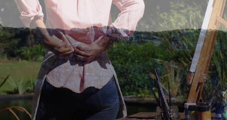 Naklejka premium Tying white apron straps, woman preparing painting in backyard by pond with easel, paint supplies